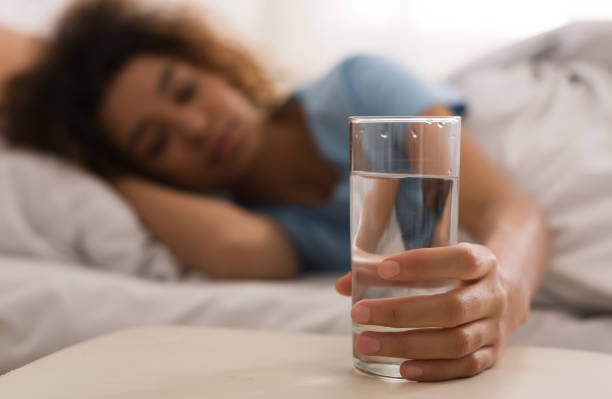 la mano de una mujer tomando un vaso de agua por la mañana - hidratación al dormir fotografías e imágenes de stock