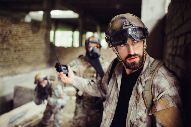 istock Handsome and bearded guy is leaning to wall and looking right. He is careful. Man has stopped his soldiers from attacking. They are waiting. 1140378993