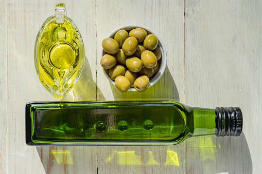 glass sauceboat with extra virgin olive oil,  fresh green olives and bottle on wooden table.