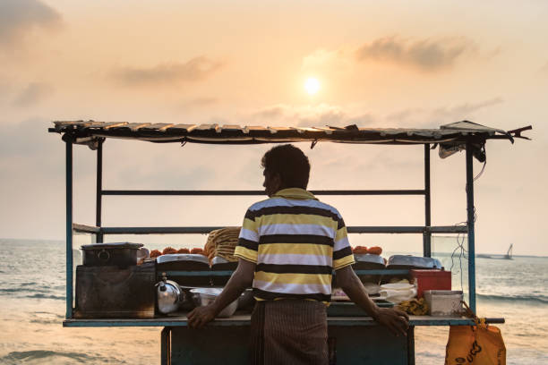 ein sri lankan männlicher verkäufer, der neben seinem stallladen auf dem galle face beach food market in colombo, sri lanka, gebratene meeresfrüchte verkauft. - pawn shop fotos stock-fotos und bilder