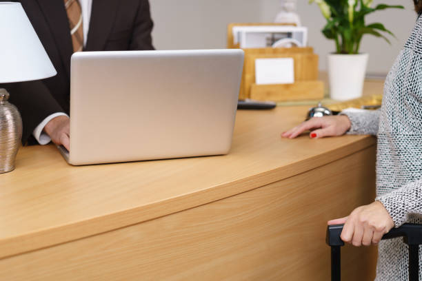 Female tourist booking into a hotel reception with her suitcase, close up view on her hands and the counter