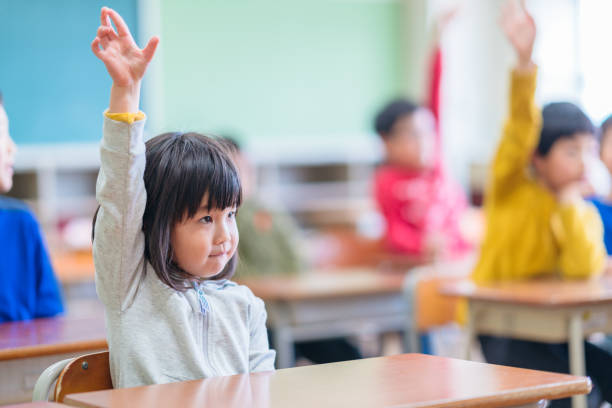 教室で手を上げるかわいい小学校女子 - 女子生徒 ストックフォトと画像