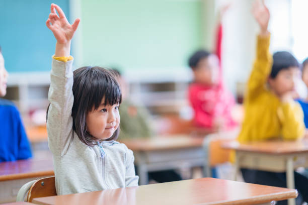 cute elementary school girl raising hand in classroom - elementary student classroom education elementary school building imagens e fotografias de stock