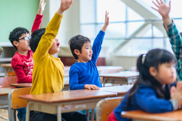 教室で手を上げている小学生たちのグループ - 小学生 ストックフォトと画像