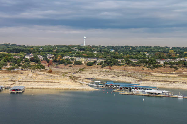 travis lake bei austin texas während einer dürre mit der wasserlinie hinunter-blick von oben mit marinas und gebäuden und einem wasserturm am ufer unter stürmischem himmel - travis county stock-fotos und bilder