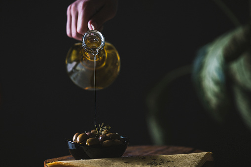 Olive oil is a natural oil obtained from olives obtained from olive tree. a picture of olive oil was taken with a bowl of olive in front of a gray background.