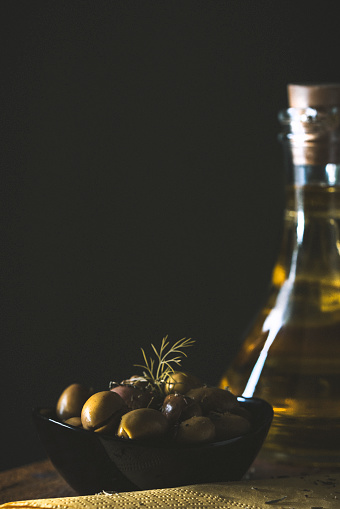 Olive oil is a natural oil obtained from olives obtained from olive tree. a picture of olive oil was taken with a bowl of olive in front of a gray background.