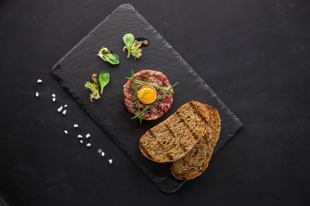 Steak Tartare with bread toasts served on a stone plate top view on black background stock photo