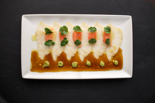 White fish carpaccio with grapefruit, soy sauce and wasabi on black background stock photo