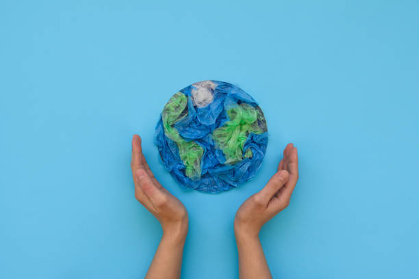hands holding planet earth made from plastic disposable packages on blue background. save the world, creative, environment pollution or world earth day concept. top view - pacote plastico imagens e fotografias de stock