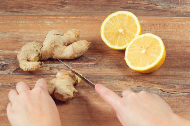 istock Female hands cut into pieces ginger root for a drink made from fresh lemon and ginger on brown wooden background. Handmade drink. 1140399142