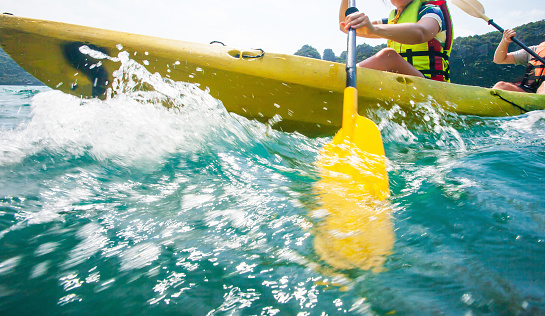 Motion blur, close shot of explorer women in life jacket paddling hard the kayak with splashes in sunny, adventure in a tropical sea. Soft focus on water.