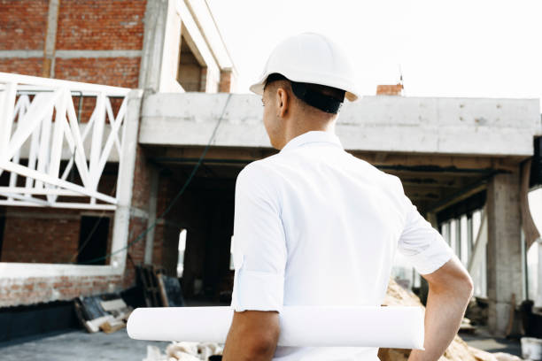 istock Back view of a young caucasian master inspecting how work is going on the building holding the plan of the building. 1140404748