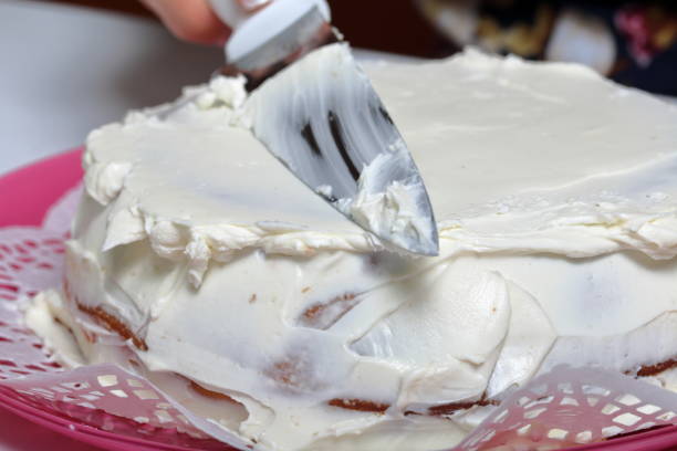 istock Baked biscuit cake. A woman smears it with white cream. 1140406238
