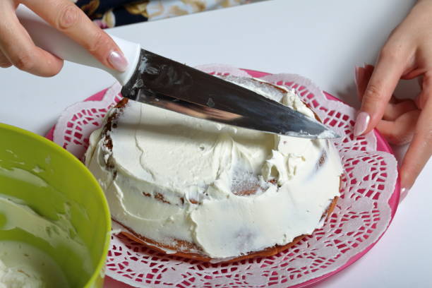 istock Baked biscuit cake. A woman smears it with white cream. 1140406242