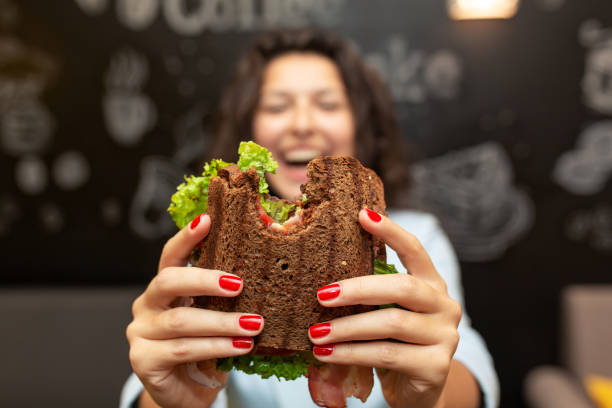istock Closeup funny blurred protrait of young woman hold bitten sandwich by her two hands. Sandwich in focus. dark background. 1140407352