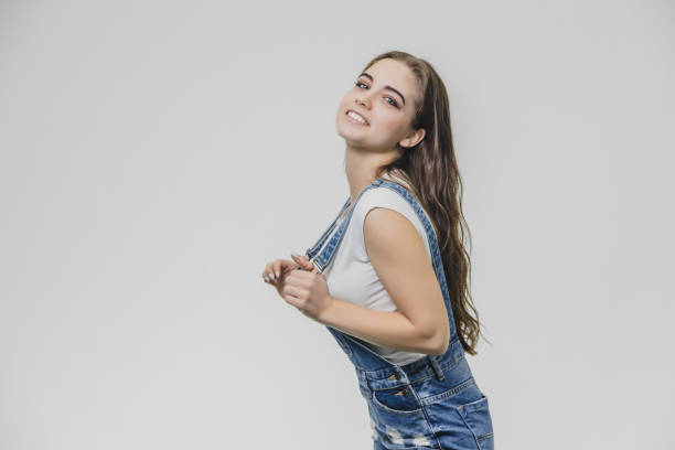 istock Young pretty student girl standing on a white background. Dressed in a denim suit and a white T-shirt. Holding his hands on the pliers from the combinator eyefully looks into the camera. 1140407390