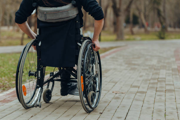 公園内の歩行中に車椅子の車輪に男性の手のクローズアップ。彼は車輪に手を握っている。 - working people physical impairment wheelchair ストックフォトと画像