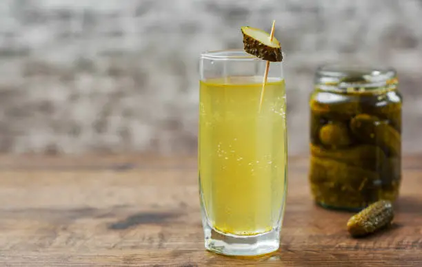 Pickle juice in glass and a can of pickled cucumbers on wooden table background