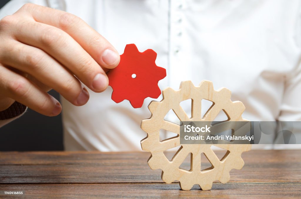 Businessman connects a small red gear to a large gear wheel. Symbolism of establishing business processes and communication. Increase efficiency and productivity. The best business formula for success Abstract Stock Photo