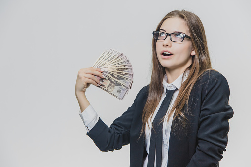 Happy excited young business woman is showing a pile of money, isolated on white background. Girl is satisfied by huge amound of bucks. Adorable businesswoman is smiling broadly wearing glasses with black rim.