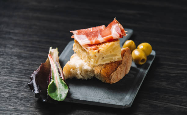 Tapa of Spanish omelette and ham closeup of a plate with some typical spanish pincho de tortilla and pincho de jamon, spanish omelette and serrano ham served on bread tortilla de patatas stock pictures, royalty-free photos & images