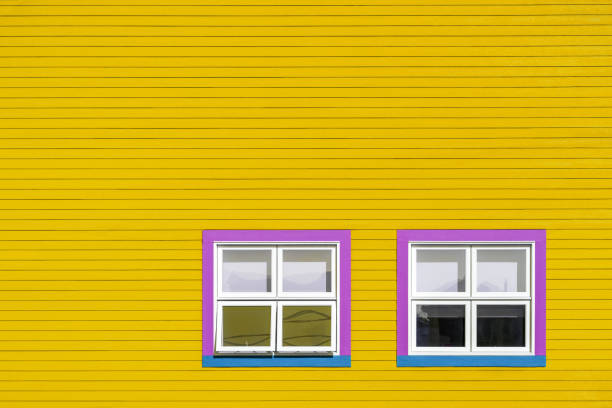 Pink, blue and white windows on a yellow wooden wall. Minimalism style of the houses of Iles de la Magdalen, Canada, in bright colours with space for text.