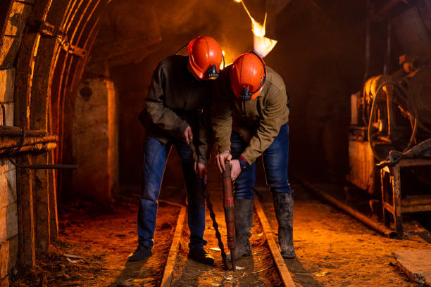 dos jóvenes en un uniforme de trabajo y cascos protectores, llevan a cabo el trabajo en la mina. mineros - minería de datos fotografías e imágenes de stock