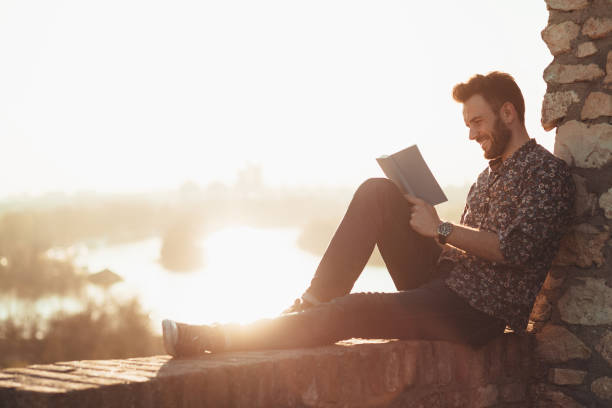 istock Young man reading a book outdoors in sunset 1140431269