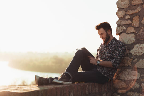 istock Young man reading a book outdoors in sunset 1140431272