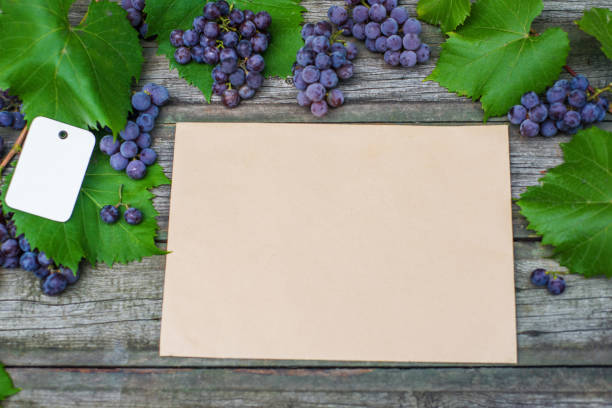 Vine with grapes and leaves on vintage rustic wooden table. Paper tag on leaves and old paper template. top view