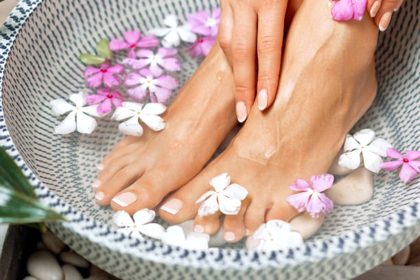 Spa treatment and product for female feet and foot spa. Foot bath in bowl with tropical flowers, Thailand. Healthy Concept. Beautiful female feet, legs at spa salon on pedicure procedure. stock photo