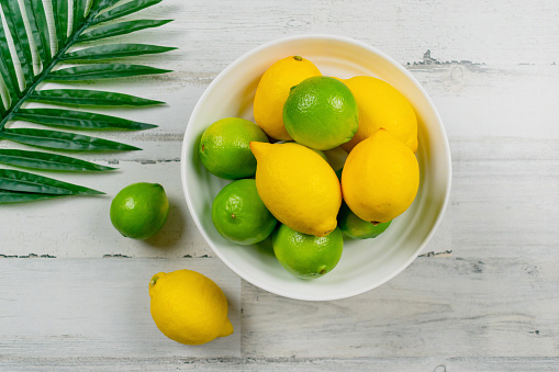 Fresh colorful lemons and limes in a white bowl on white wood surface