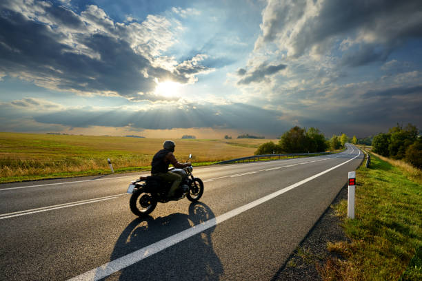 moto conduisant sur la route asphaltée dans le paysage rural au coucher du soleil avec des nuages dramatiques - motorcycle road journey travel photos et images de collection