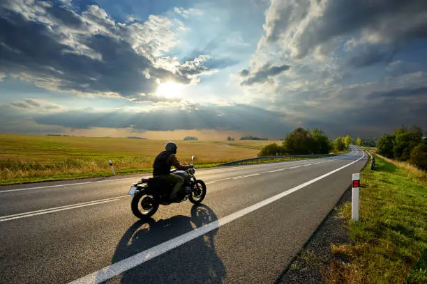 Photo of Motorcycle driving on the asphalt road in rural landscape at sunset with dramatic clouds