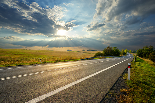 Empty asphalt road in rural landscape at sunset with dramatic clouds