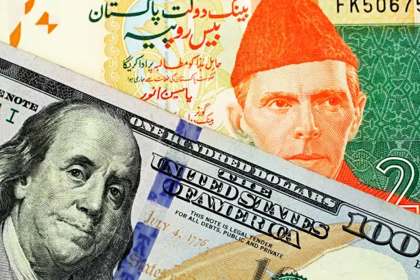 Photo of A close up image of a Pakistani rupee bank note with an American one hundred dollar bill