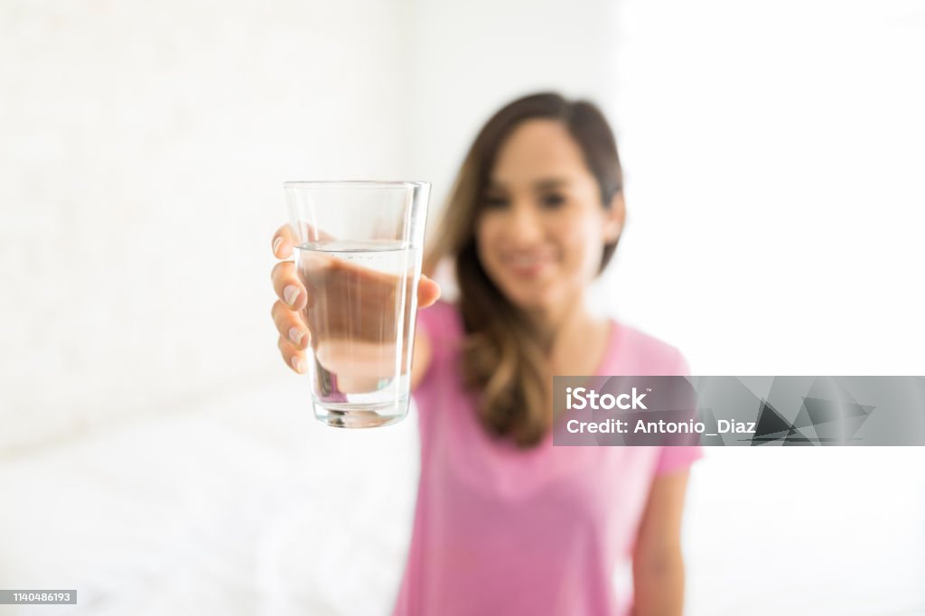 Water Helps To Maintain Organ Health Mid adult woman holding glass of clean drinking water at home 30-39 Years Stock Photo
