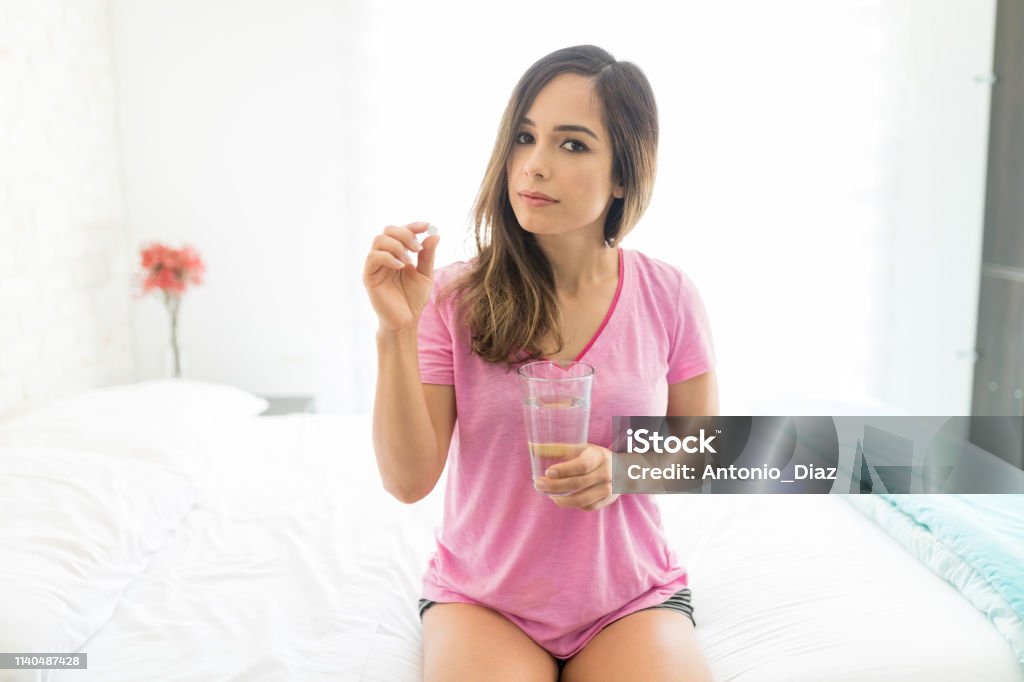 Woman Having Prescribed Medicine Portrait of woman taking tablet while suffering from bad health and relaxing on bed Healthcare And Medicine Stock Photo