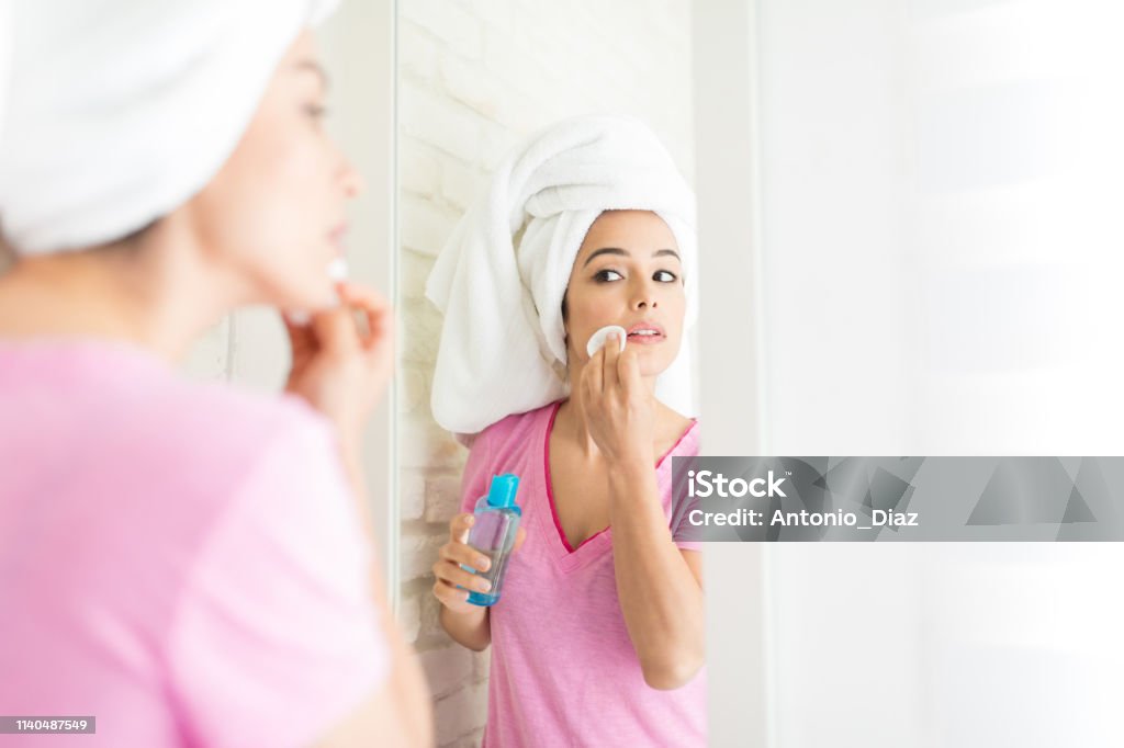 Keeping Her Skin Perfect Woman looking at herself in mirror while applying essential oil with cotton pad Cotton Pad Stock Photo