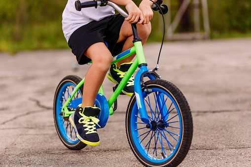 un niño en zapatillas de deporte que pedalear un dos ruedas en el asfalto en el verano. sólo los pies en los pedales de la bicicleta photo