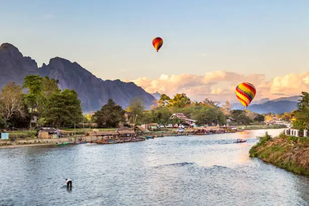 Colorful hot air balloon floating above the river in Vang Vieng city , Laos at sunset