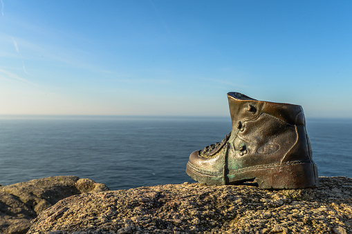 A cast bronze boot on the rocks at the end of camino de santiago - Finisterre