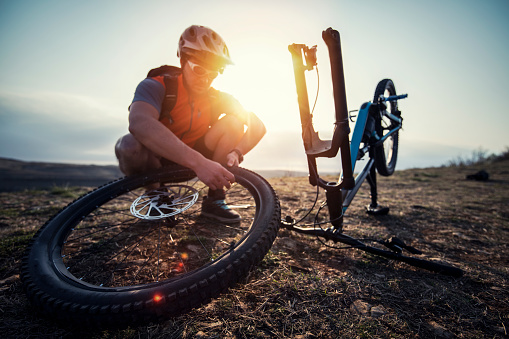 Mountain biker Repairing A Flat Tire on mountain peak at sunrise.