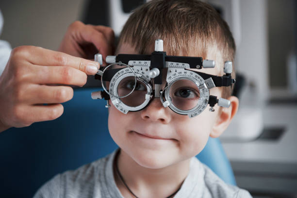 réglage de l’intrusion. petit garçon avec le phoropter ayant l’essai ses yeux dans le bureau du médecin - lunettes photos et images de collection