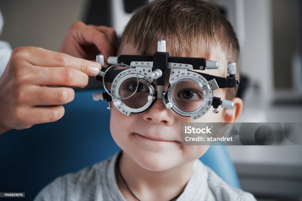 Tuning the intrument. Little boy with phoropter having testing his eyes in the doctor's office Tuning the intrument. Little boy with phoropter having testing his eyes in the doctor's office. Child Stock Photo
