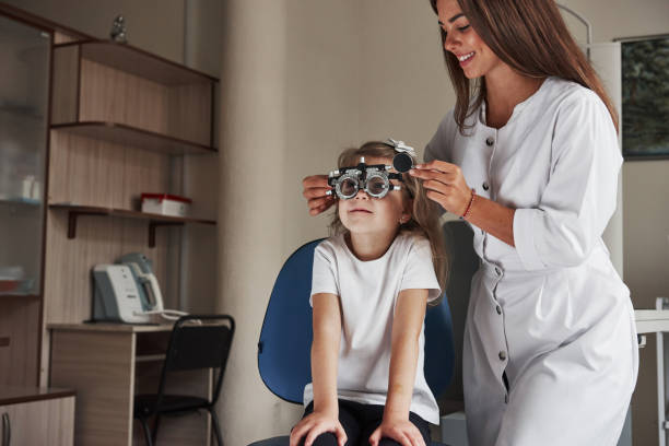 作業中です。クリニックに座って、彼女の目がテストされている眼鏡の小さな女の子 - patient happiness cheerful optometrist ストックフォトと画像