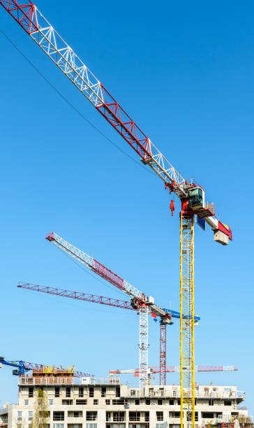 istock Five large tower cranes above a concrete building under construction against blue sky. 1140526724