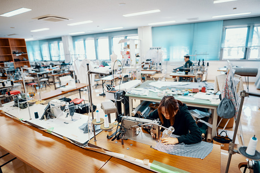 Mid adult woman working at a sewing machine in textile studio creating denim products in Japan