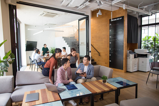 2 Hong Kong business men and 2 Hong Kong business women exchange conversation on sofa using wireless devices in coworking area